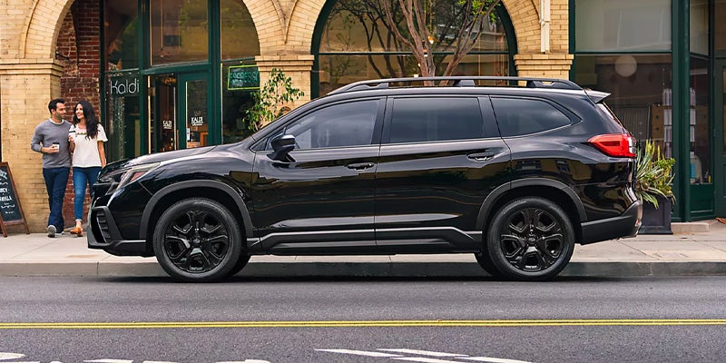 Black SUV with roof rails parked on a city street, a couple walks on the sidewalk in the background.
